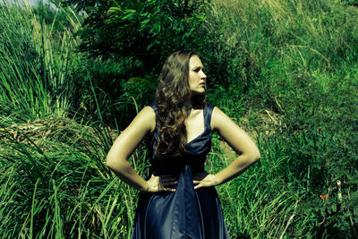 Young woman standing with arms akimbo by plants