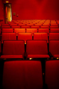 Bright red auditorium with rows of empty red cloth covered seats and open exit door