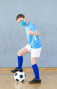 Portrait of boy wearing mask standing by soccer ball