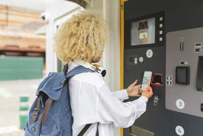 Woman using ticket vending machine scanning qr code through smart phone