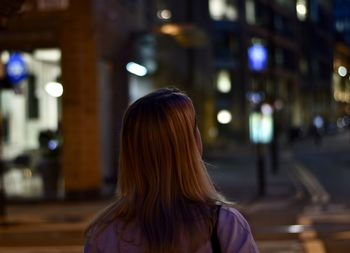 Rear view of woman standing in illuminated city at night