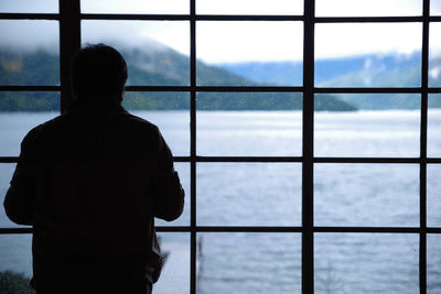 Rear view of silhouette man looking at window