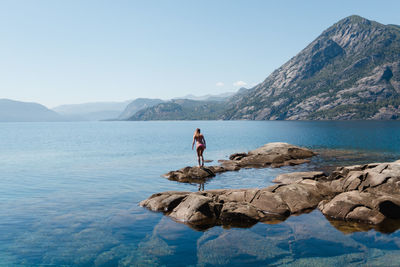 Woman standing on rock by sea against clear sky