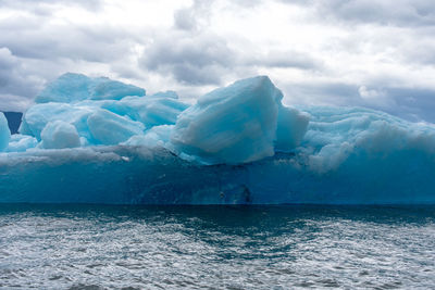 Icebergs in sea against cloudy sky