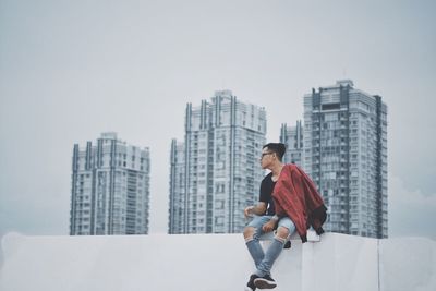 Full length of man sitting on city against sky