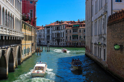 Boats in canal amidst city against clear sky