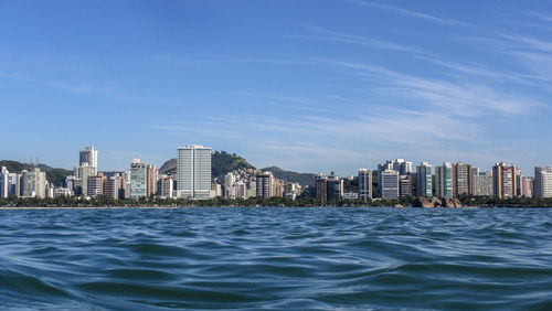 Sea by buildings in city against blue sky