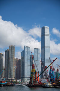 Cranes by buildings against sky