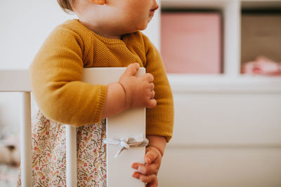 Midsection of boy holding baby standing against wall