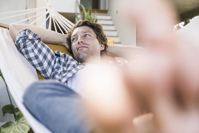 Mid adult man resting in hammock with hands behind head at home