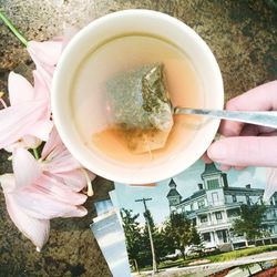 Cropped image of hand holding tea cup by photographs and flowers