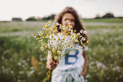 Woman holding white flowers while standing on field