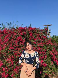 Portrait of woman wearing face shield to protect covid19 standing by flowering plants against sky 