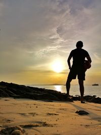 Rear view of silhouette man standing on beach during sunset