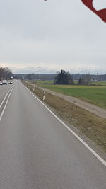 Road passing through field against sky