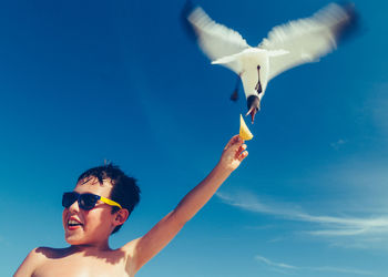 Low angle view of shirtless man feeding bird against blue sky