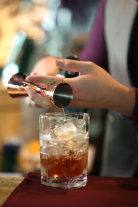 Close-up of hand pouring drink in glass on table