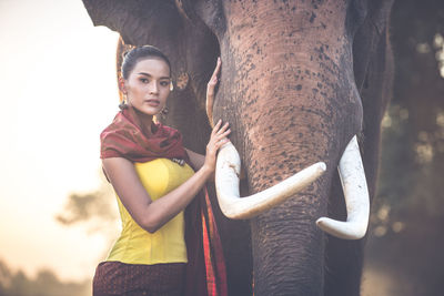 Portrait of young woman standing by elephant in forest