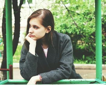 Thoughtful woman leaning on green railing at park