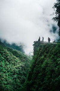 People on cliff against cloudy sky during winter