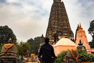 Rear view of man meditating while sitting outside temple