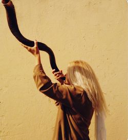 Woman blowing shofar while standing against wall