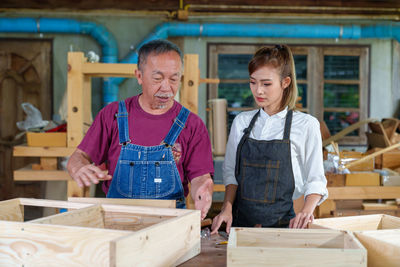 Tutor with female carpentry student in workshop studying for apprenticeship at college ,