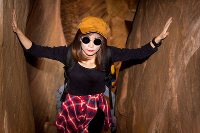 Portrait of young woman wearing sunglasses standing against wall