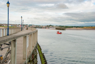 A small red fishing boat passes a pier on a calm day.