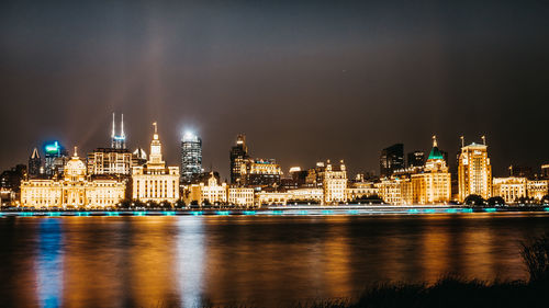 Illuminated buildings by river against sky at night