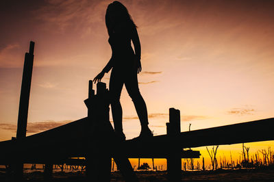 Silhouette woman standing on pier at beach against sky during sunset