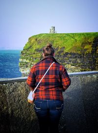 Rear view of young woman looking at view while standing against clear sky