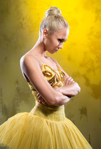 Ballerina wearing costume with arms crossed standing against yellow background