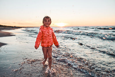 Playful little girl splashing a water towards camera enjoying a free time over sea on a sand beach