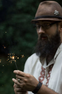 Portrait of young man burning sparkler while standing in forest