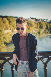 Young man wearing sunglasses standing against railing