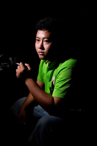 Portrait of young man sitting against black background