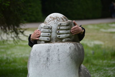 Person touching statue while hiding behind it in park