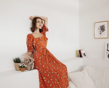 Young woman sitting against wall at home