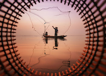 Silhouette people fishing by lake against sky during sunset