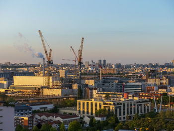 High angle view of cranes and buildings against sky during sunset