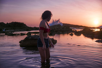 Woman standing at beach against sky during sunset