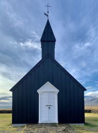 Exterior of black church on field against sky