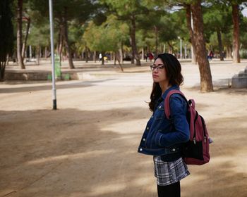 Side view of young woman standing against trees