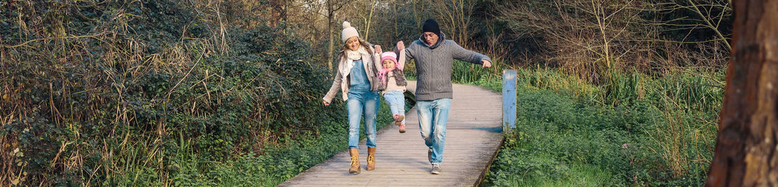 Panoramic view of parents holding cute daughter while walking on footpath in forest