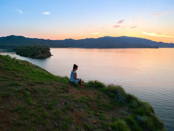 Man sitting on lake against sky during sunset