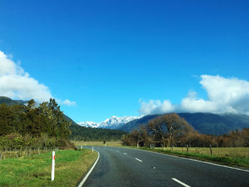 Road leading towards mountains against blue sky