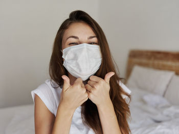 Woman wearing mask while sitting on bed at home