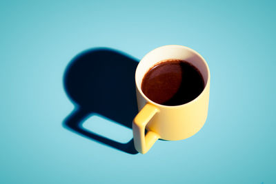 Fresh turkish coffee in a yellow cop with hard shadow on blue background.