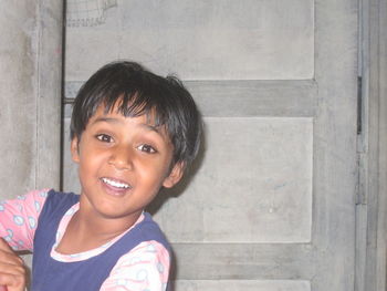 Close-up portrait of smiling girl standing against wall